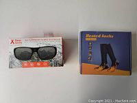 Box of Bear Grylls Waterproof Video Eyewear and box of heated socks for winter on white background, both items new in box.