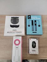 EMS Muscle Toner box, CAHQT Digital Jump Rope box, HQHQQ ZERO 9 Electric Fan box, Fitness Tracker box arranged on wooden surface.