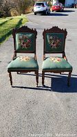Front view of both antique needlepoint upholstered dining chairs placed side by side showing floral upholstery and wooden frames