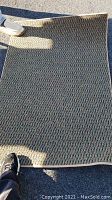 Photo of larger woven multicolor area rug lying outdoors with shadow and sunlight effects.