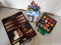 Overview image showing the Nick Williams sports figurine in box, vintage Belgian Aramith billiard balls in original green box, wooden backgammon set in open brown case, and two decks of Mack playing cards.