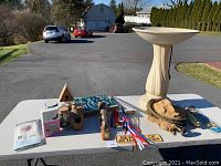 Photo of electric bird bath, wooden decorations, beekeeper hat, flags, and other items on display table