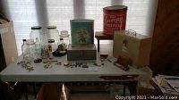 Full view of the lot on table showing all items including glass jars, metal tins, boxes, pins, watch pouch.