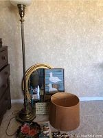 Photo showing brass floor lamp without shade, oval gold-trimmed mirror, wooden seagull artwork, flower bowl, turtle pen holder, decorative items and lampshade on floor.