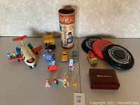 Full lot with Fisher-Price airplane, die-cast cars, frisbees, Disney figurines, Ringamajigs container, and Disney Vacation Club box visible
