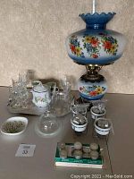 Wide shot showing oil lamp, multiple glassware sets, silver tray, porcelain containers and other small decor items grouped, illustrating lot contents