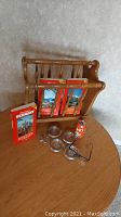 Photo showing solid wood magazine holder with Baedeker guide books for Germany, Austria, and Switzerland, Uno dice game collectible soda can bank, four Monopoly game pieces, four silver plate crystal coasters, and vintage eyeglasses on a wooden table.