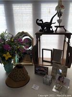 Full view of lot showing wooden magazine table, lamp with dual pheasant statues and painted glass shade, mirror, floral arrangement, and smaller decor items such as frames and lampshades