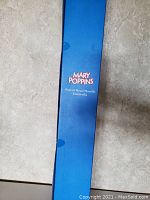 Blue box standing upright on floor with Mary Poppins branding and text describing the item as Parrot Head Handle Umbrella.