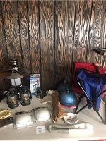 Photo of outdoor lighting items, gas lanterns, metal hand warmers, seats, and miscellaneous lighting items against wood background