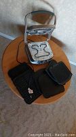 Panini press open showing inside top and bottom heating elements and heating plate attachments spread around it on a round wooden table.