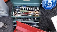 Green toolbox filled with various hand tools including sockets, ratchets, wrenches, and screwdrivers.