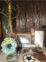 Wide shot showing the tree man sculpture with facial features, outstretched branches, and birds. Surrounding items include framed prints, a rag wreath, a disco ball, and wall light parts.