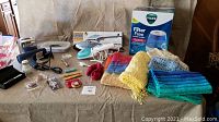 Photo showing entire lot with humidifier in box, two fabric steamers, hair dryer, and scarves arranged on a cloth surface.