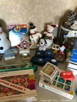 Photo shows an assortment of vintage Christmas ornaments and decorations on a surface. Includes a 3.5ft artificial Christmas tree, two snowman figurines, multiple boxes of ornaments, a Snoopy figurine, and a gingerbread house decoration