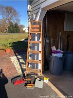 Full view of the 6FT wooden ladder standing against wall outside with tools on ground in front.
