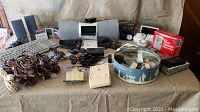 Full lot overview showing Sirius XM satellite radio receiver, computer keyboard, speakers, cords, electrical outlets, and boxed micro cassette recorder.