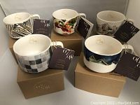 Five Starbucks collector mugs displayed on and beside their original cardboard boxes with original tags attached to each mug. Showing set numbers 1,2,3,6,7 out of 8 in the series.