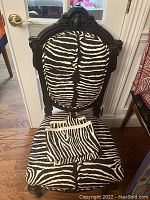 Front view of chair showing carved wooden frame and zebra-print upholstery with fabric remnants on seat