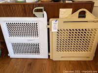 Two child safety gates, white Safety 1st and beige Fisher Price, placed side-by-side on wooden floor, showing mesh panel designs and handles.