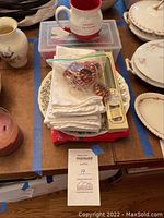 Stack of white cotton napkins with napkin rings in plastic bag on top, Santa's Favorite ceramic mug with red inside, and the Johnson Brothers Merry Christmas decorative plate partially visible underneath