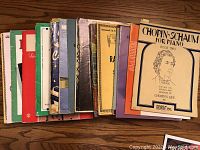Fifteen piano sheet music books displayed horizontally to show spine and covers, a mix of classical and popular pieces including Chopin-Schaum.