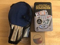 Portable ping pong paddle in mesh bag alongside two ping pong balls still in plastic packaging.