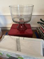 Lot showing red base glass trifle bowl on top of a red square box, mandolin slicer in front.