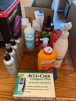 Overview of multiple bottles including antibacterial soaps, medicated body powder, leather cleaner bottles, and blood glucose meter box on wooden surface.