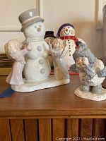 Multiple snowmen and angel figurines on wooden surface including ceramic snowman and two angels