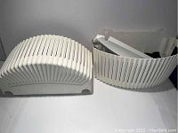 Pair of curved white wall planters, showing the outer slatted design on a white surface.