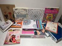 Photo showing various art books and activity kits arranged on table including craft kit box, coloring books, a book on drawing, and the blue briefcase at right end