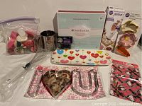 Lot contents showing various baking utensils including whisk, flour sifter, cookie cutters, decorated tray, American Girl boxed baking set, unopened gift bags, and cupcake decorations