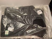 Full view of the set of four black floor mats wrapped in protective plastic packaging showing the texture and shape.