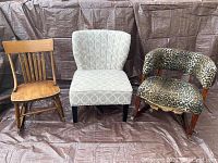 Three chairs together: wooden child's rocking chair, gray patterned slipper chair, and animal print rocking chair