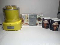 Yellow Cuisinart ice cream maker with clear lid, packaged molecular gastronomy kit box, and two unopened cans of ice cream starter mix.