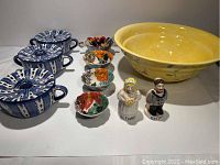 Full view of all kitchen ceramic items including large yellow floral serving bowl, three blue and white Portuguese soup terrines, floral measuring cups, and vintage bride and groom salt and pepper shakers.