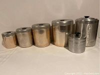 Six vintage metal kitchen canisters arranged from smallest to largest showing four rose-colored nesting canisters and two larger silver canisters.
