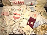 Large assortment of vintage linens including hand towels, pillowcases, handkerchiefs, and tablecloths, displaying various embroidery and lace details in neutral and pastel tones.