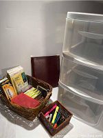 Baskets with cards, labels, pens, and highlighters next to a stack of storage drawers and a chair