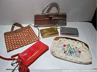 Photo of six purses and handbags including large silver Whiting & Davis handbag, small gold and silver pouches, red wristlet, brown cutout leather bag and vintage floral clutch.
