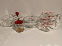 Full view of all items: two Pyrex measuring cups, one Pyrex bowl with lid, vintage glass chopper with red lid and handle, pressed glass bowl.