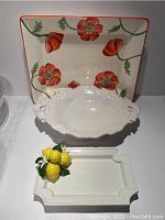 Showing three ceramic items including poppy floral platter, white ornate serving bowl, and white ceramic platter with lemon decoration