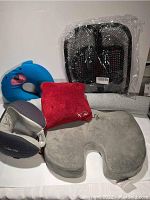 Various travel pillows in different styles, including ComfiLife gray pillow, red plush pillow, blue dolphin shaped pillow, gray and white pillow, gray halo neck pillow, and a black mesh pouch in the background.