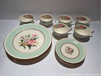 Top view of six dinner plates, six tea cups, and five saucers showing floral design with mint green border and gold accents.