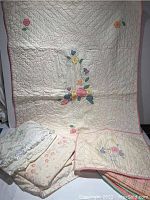 Full view of the quilt propped up with matching pillow and floral bedding with embroidered table runner beside it
