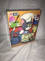 Front view of the puzzle box in original shrink wrap, showing Tom as a chef icing a cake, Jerry mouse beside the cake, '100' piece count and Golden brand logo.