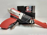 Photo showing NES Zapper light gun wrapped with cable and the Mario Bros game cartridge in sleeve.