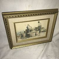 Framed print showing two fishermen working by the water, with large wooden baskets. Gold carved frame and linen matting visible.