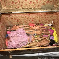 Wide shot of the open wooden toy box showing multiple Barbie dolls, some hair tangled and messy, some naked, plus doll clothing and accessories at the bottom.